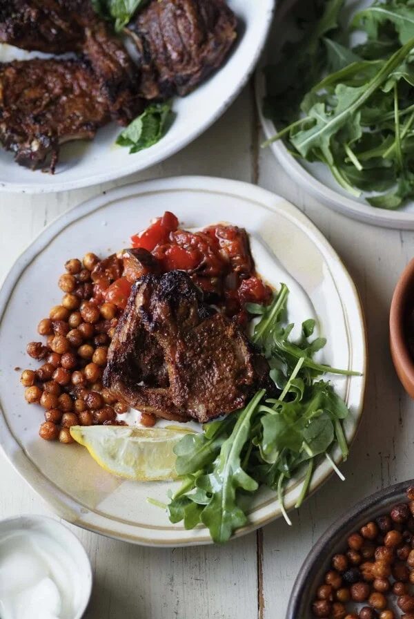 air fryer lamb chops with tomato aubergine stew and rocket on a white plate.