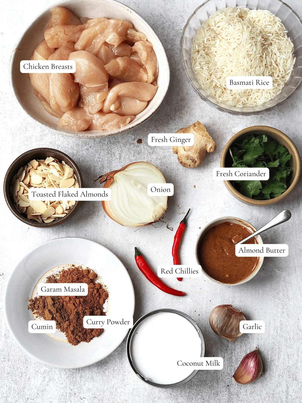 Ingredients to make an Almond Butter Chicken Curry on a grey background.