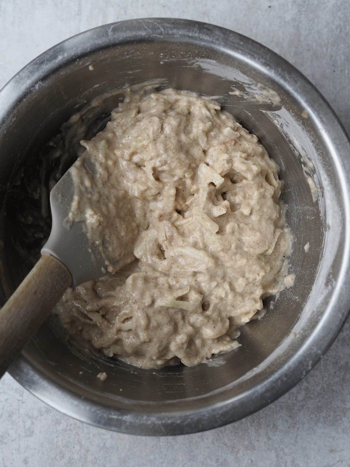 Adding grated apples to the fritter batter with spoon in metal bowl.