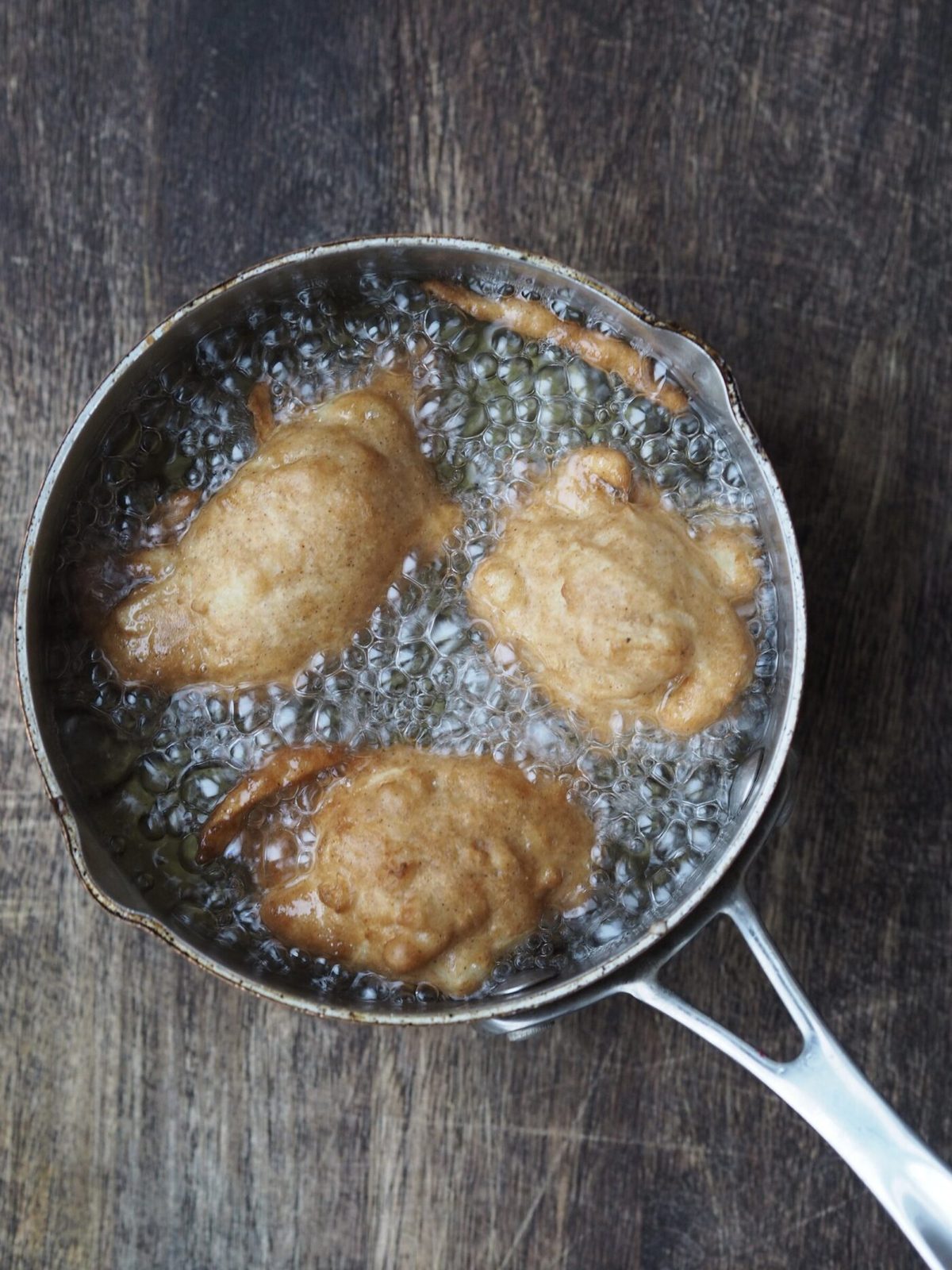 Applesauce fritters cooking in pan of hot oil.