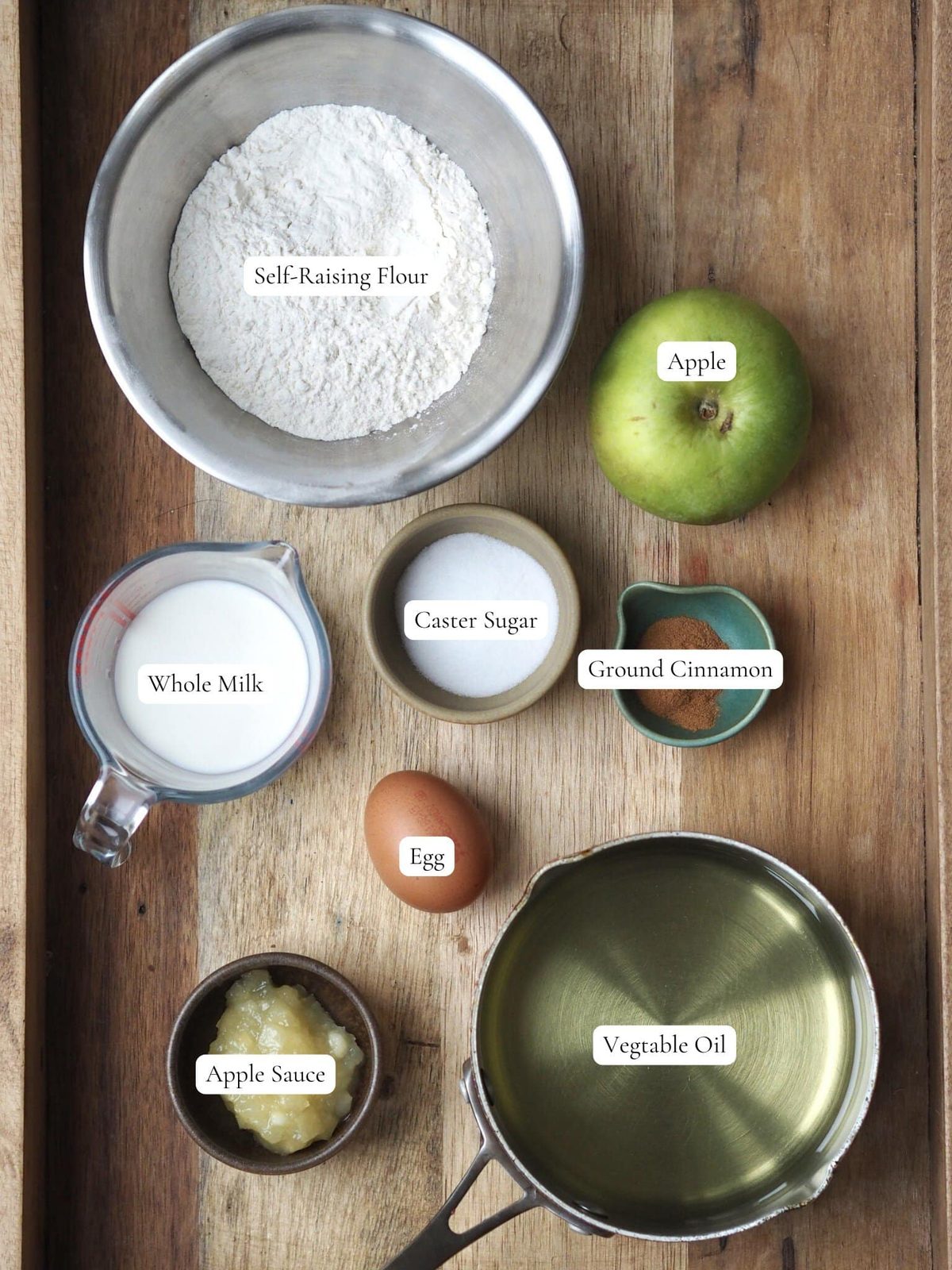 Flour, apple, sugar, applesauce, and other fritter ingredients on wood table.