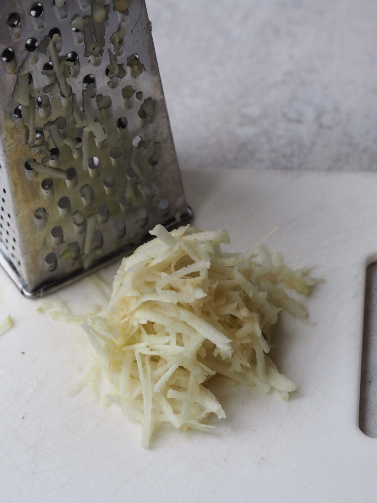 Freshly grated apple next to box grater on cutting board.