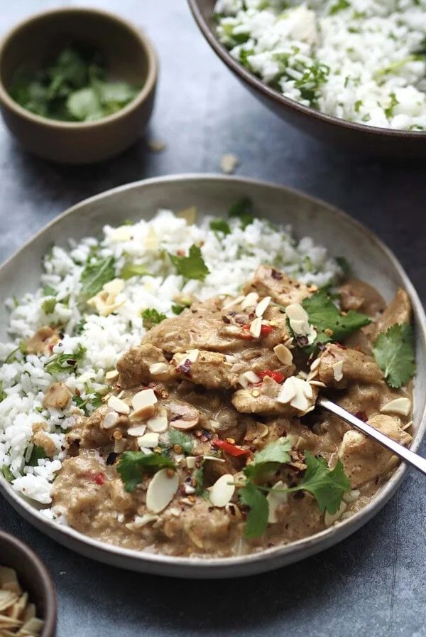 Grey bowl of white rice with coriander and chicken curry topped with toasted almonds.
