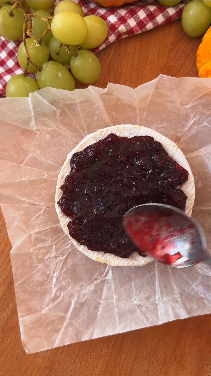 Topping brie with cranberry sauce using spoon.
