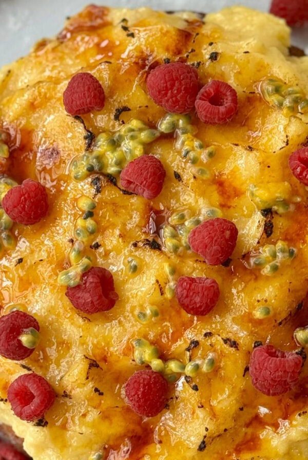 whole creme brulee cake decorated with raspberries and passionfruit.