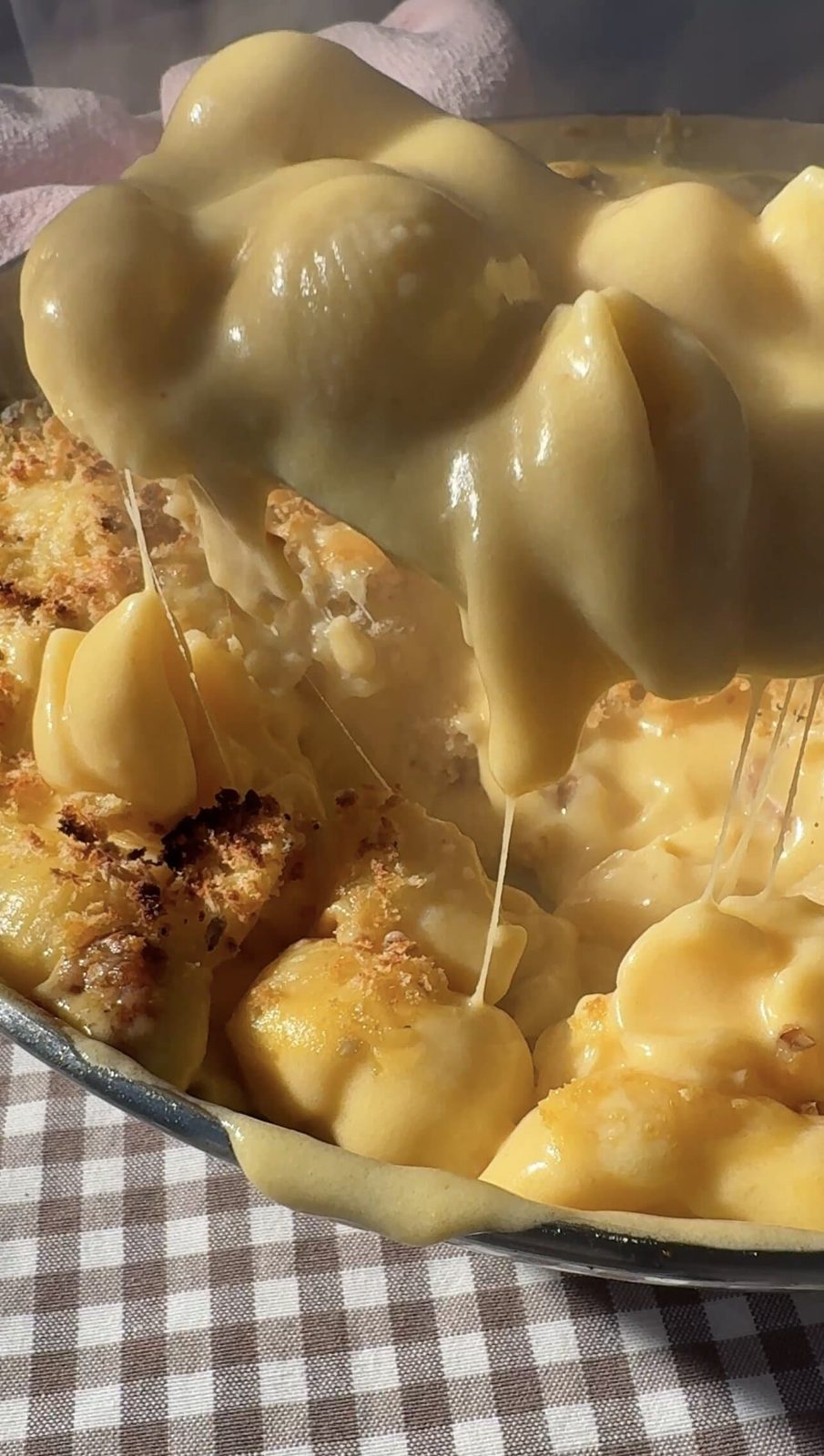 Scooping Gouda mac and cheese from a pan.