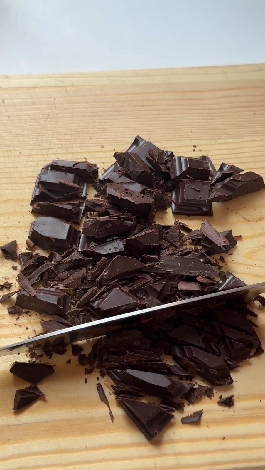 Chopping dark chocolate into chunks with knife on wood cutting board.