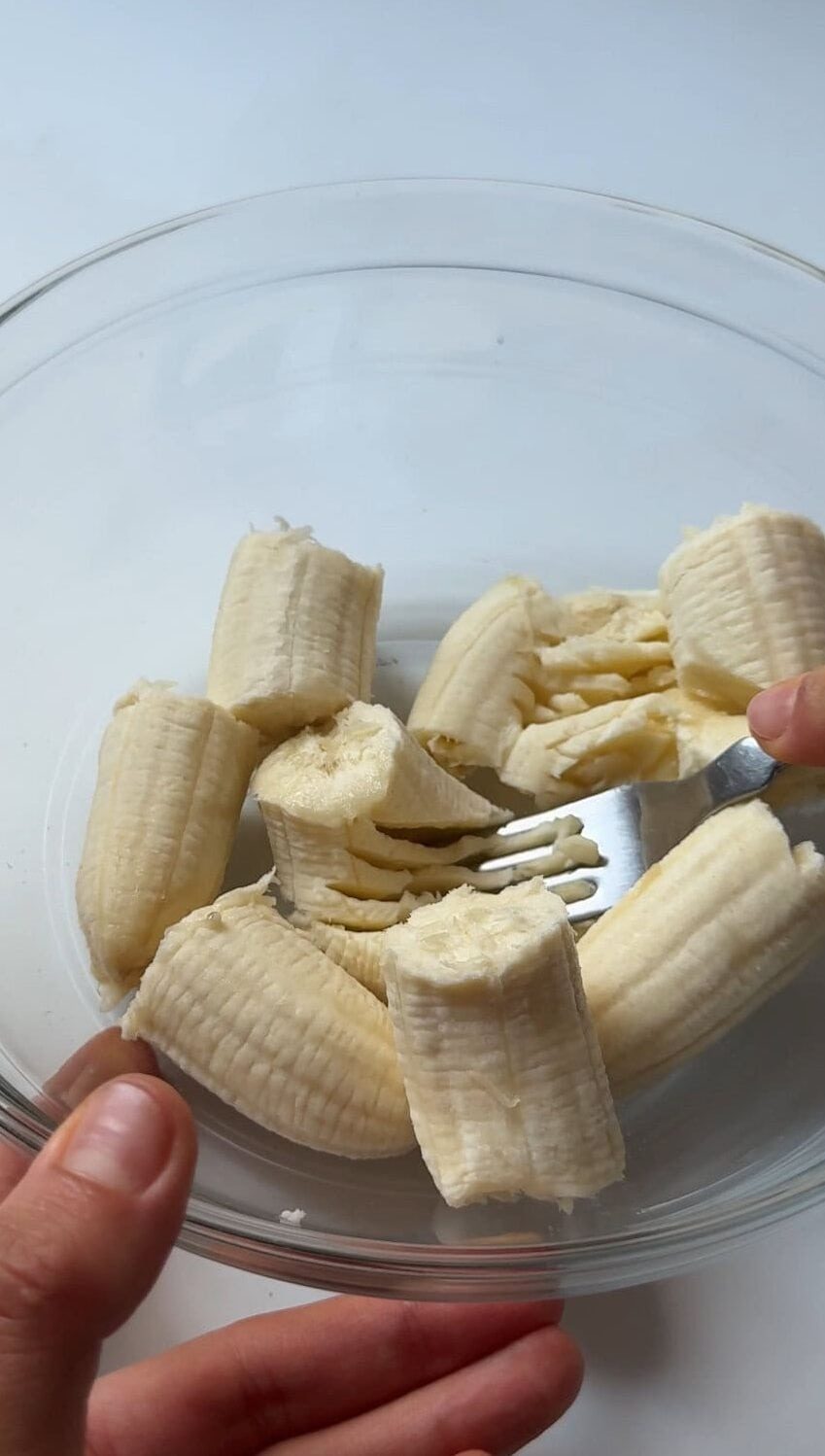 Mashing bananas with a fork in glass bowl.