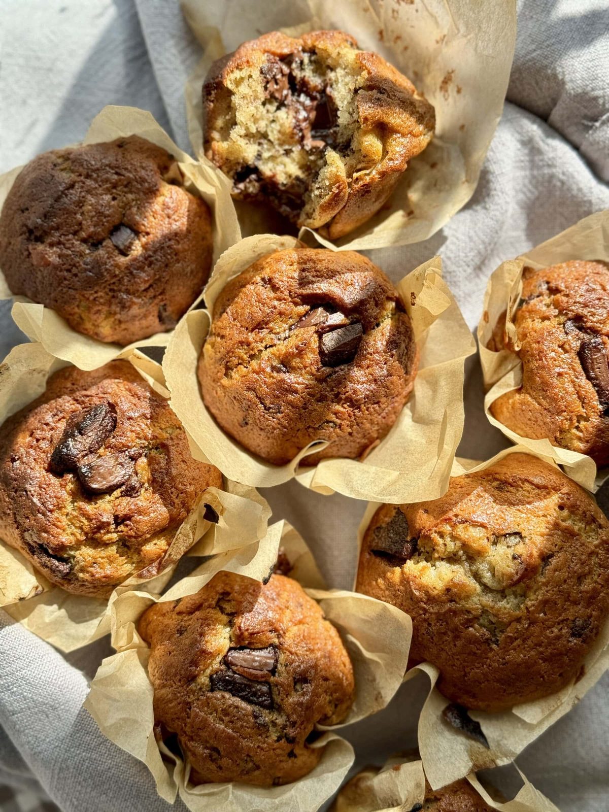Banana chocolate chunk muffins in paper piled on towel.