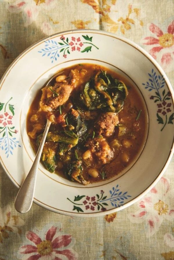 Vintage bowl of sausage and bean stew on a red floral tea towel.