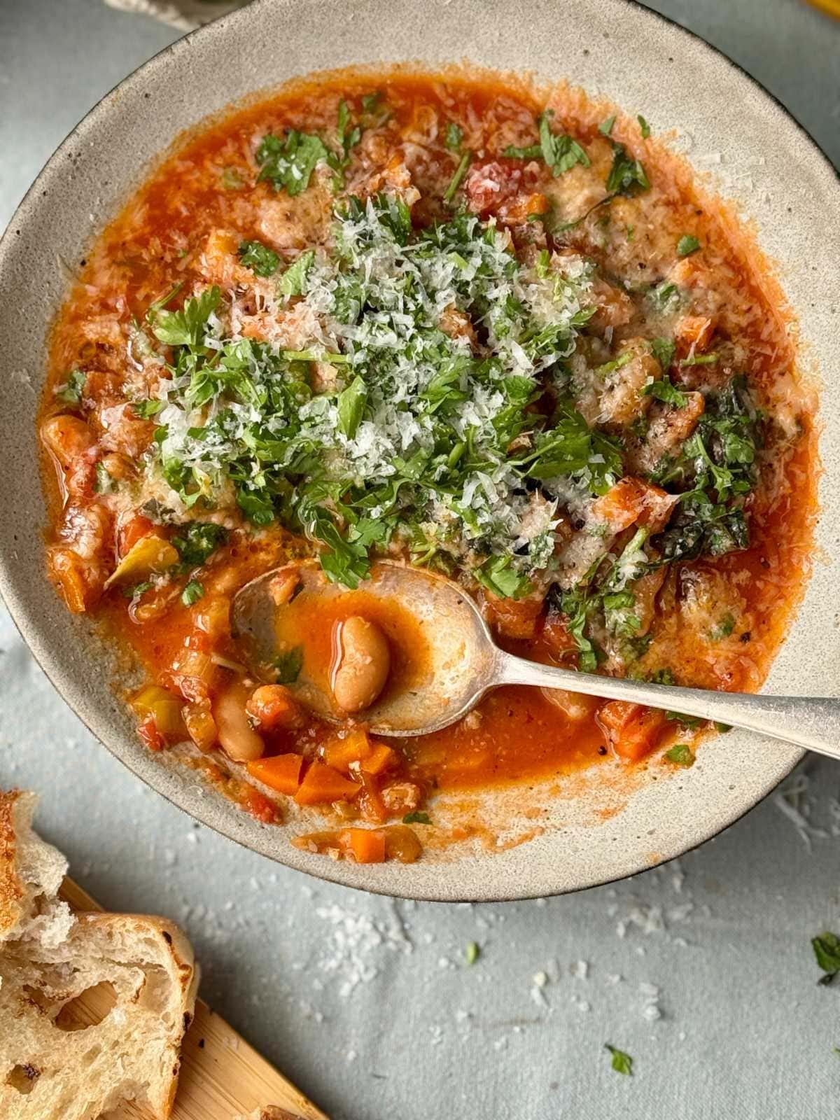 spoon in bean stew in a bowl with bread on the side.