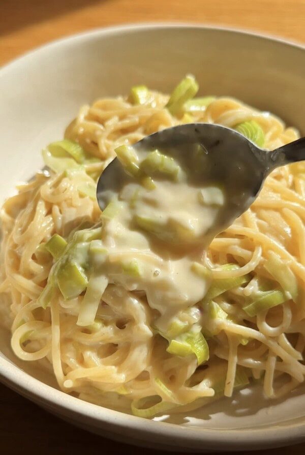 spooning sauce over leek pasta with a spoon in a white bowl