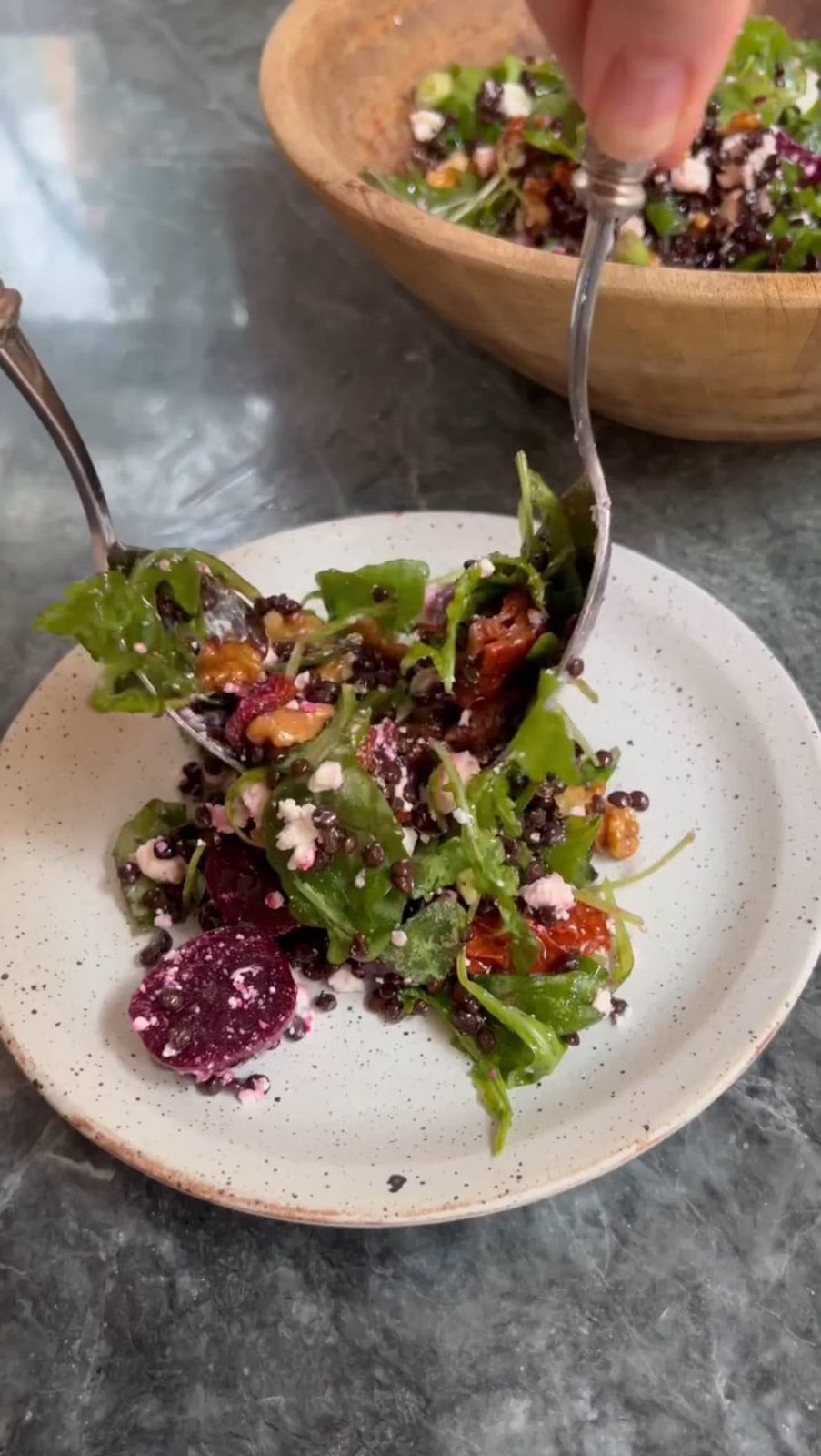 Tossing beetroot and feta salad dressed with vinaigrette with spoons.
