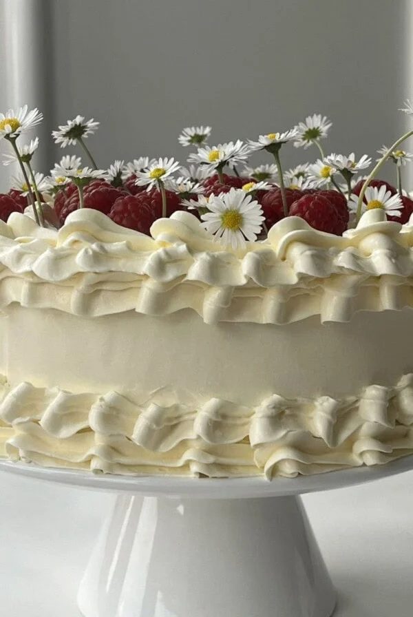 white chocolate raspberry cake on a white cake stand.