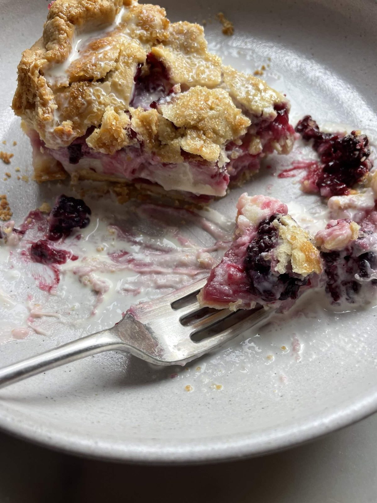 Partially eaten blackberry cream cheese pie on plate with a fork.