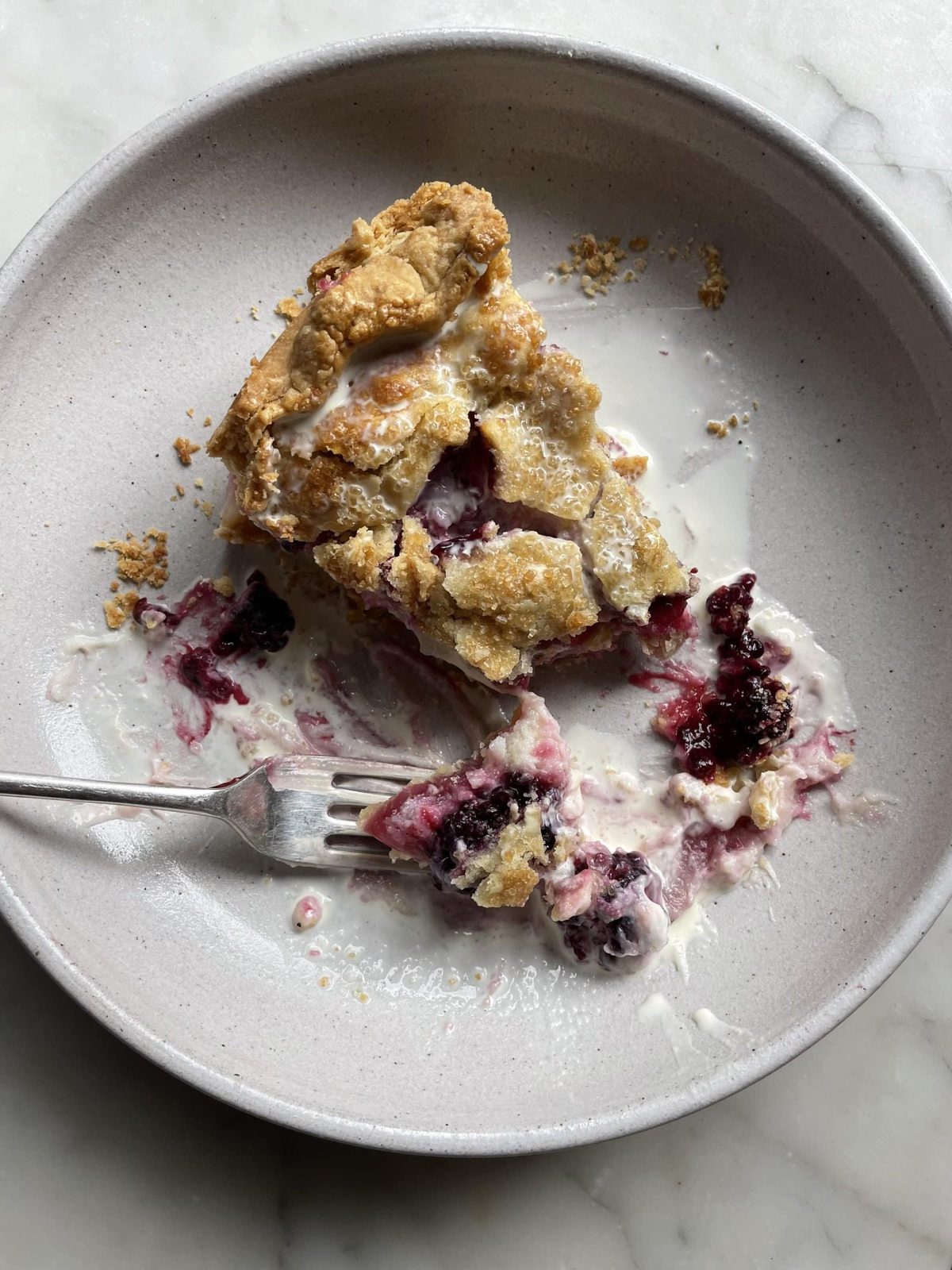 Slice of blackberry pie with cream on plate with fork.