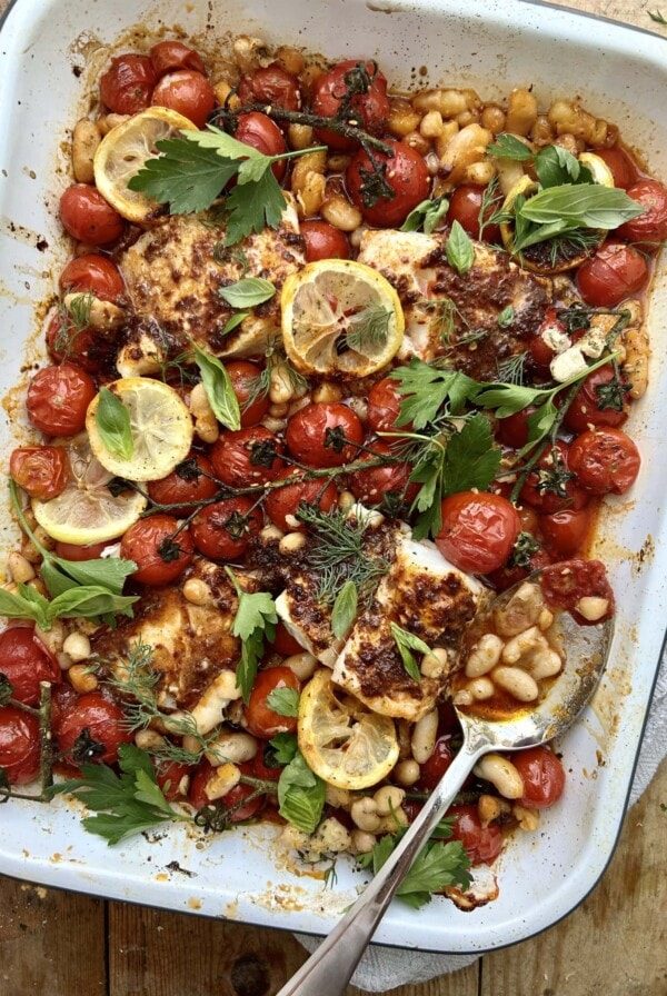 White tray of roasted tomatoes, beans and harissa cod.