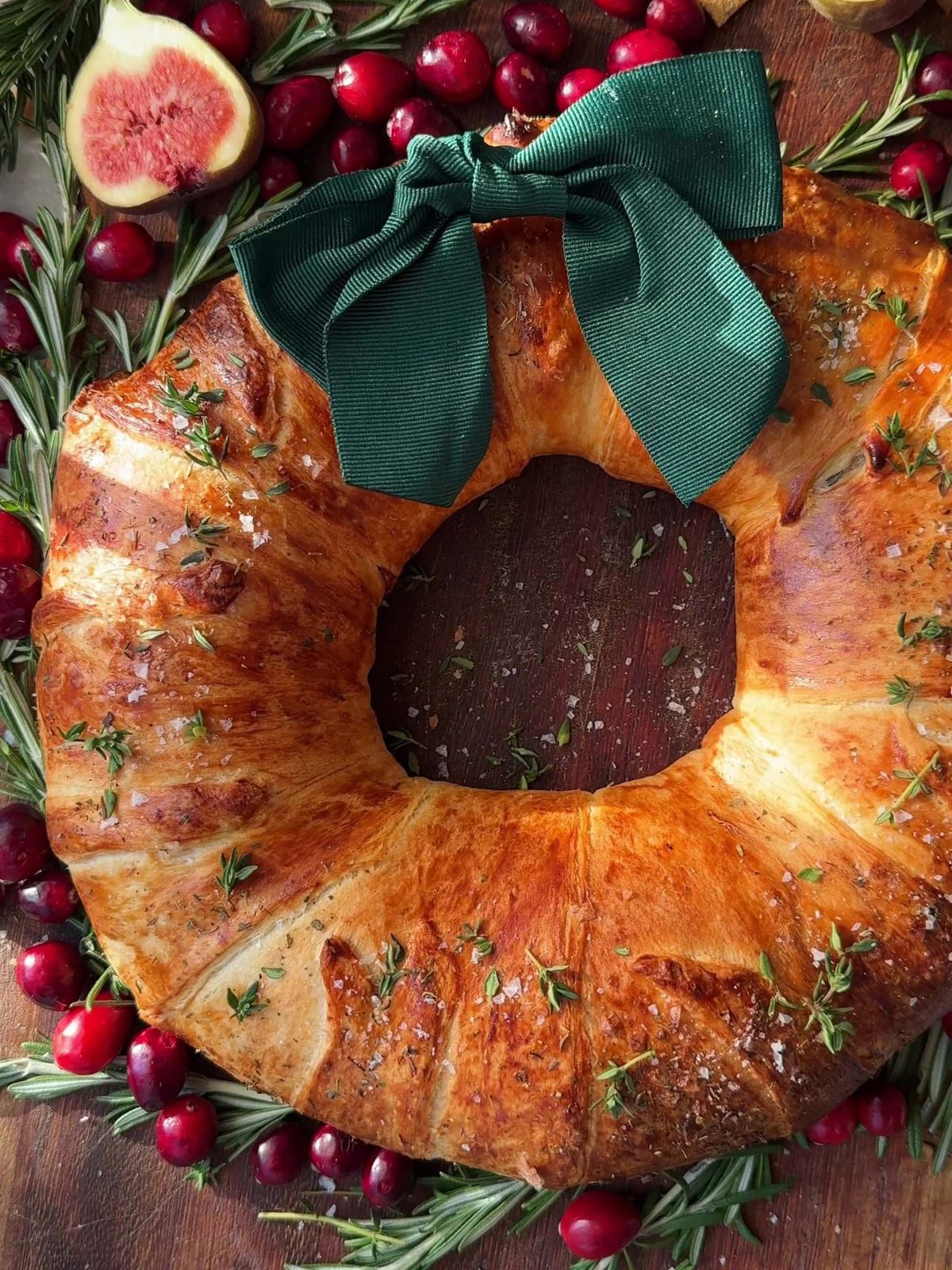 Brie Crescent Wreath with fresh figs, cranberries, and ribbon on a board.