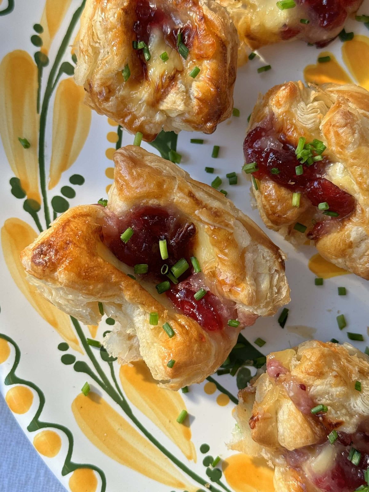 Fresh chives on brie puff pastry bites with cranberry sauce.