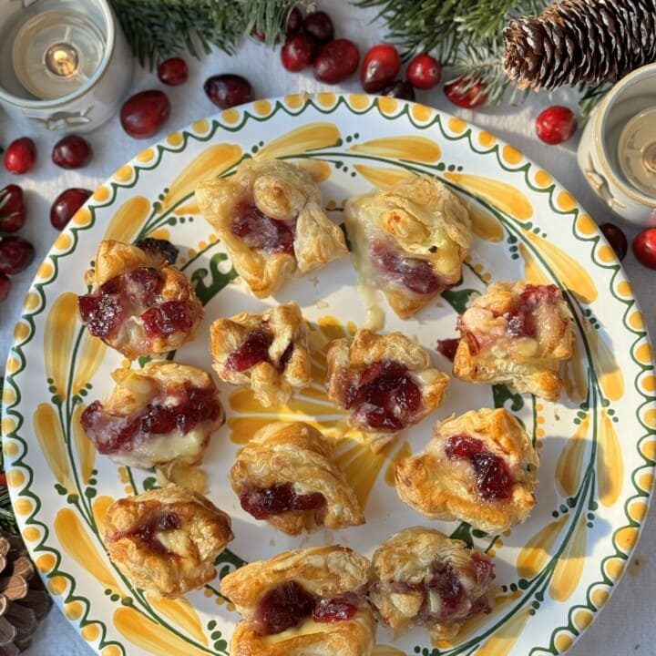 Brie puff pastry bites with cranberry sauce arranged on plate.