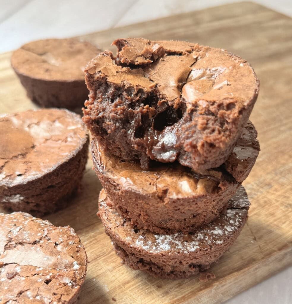 A stack of brownie bites on a wooden chopping board.