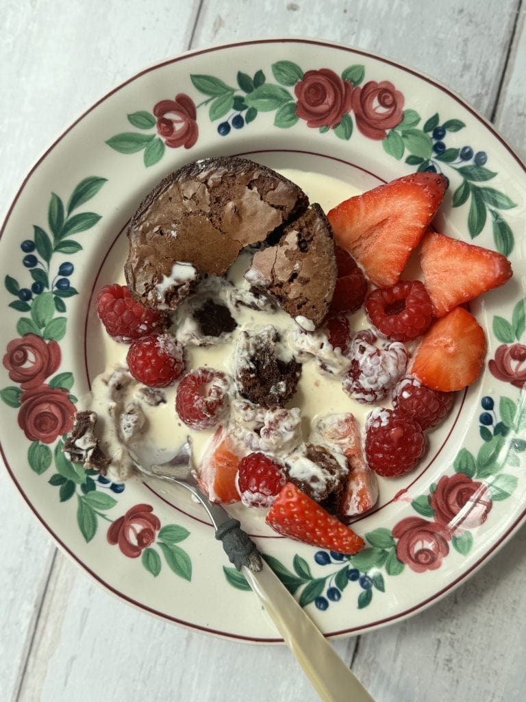 A brownie bite in a floral bowl with cream and berries.
