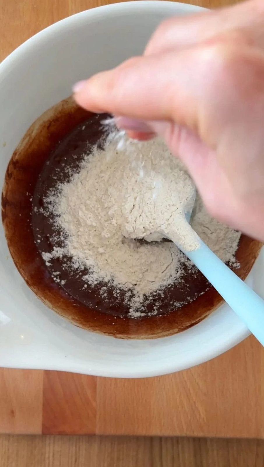 Adding flour to brownie bites batter in bowl.