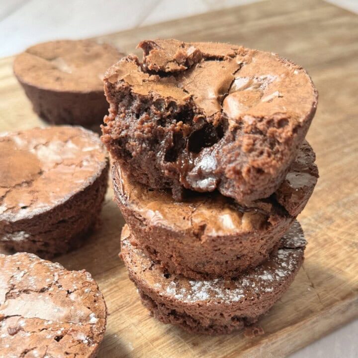 a stack of brownie bites on a wooden chopping board.
