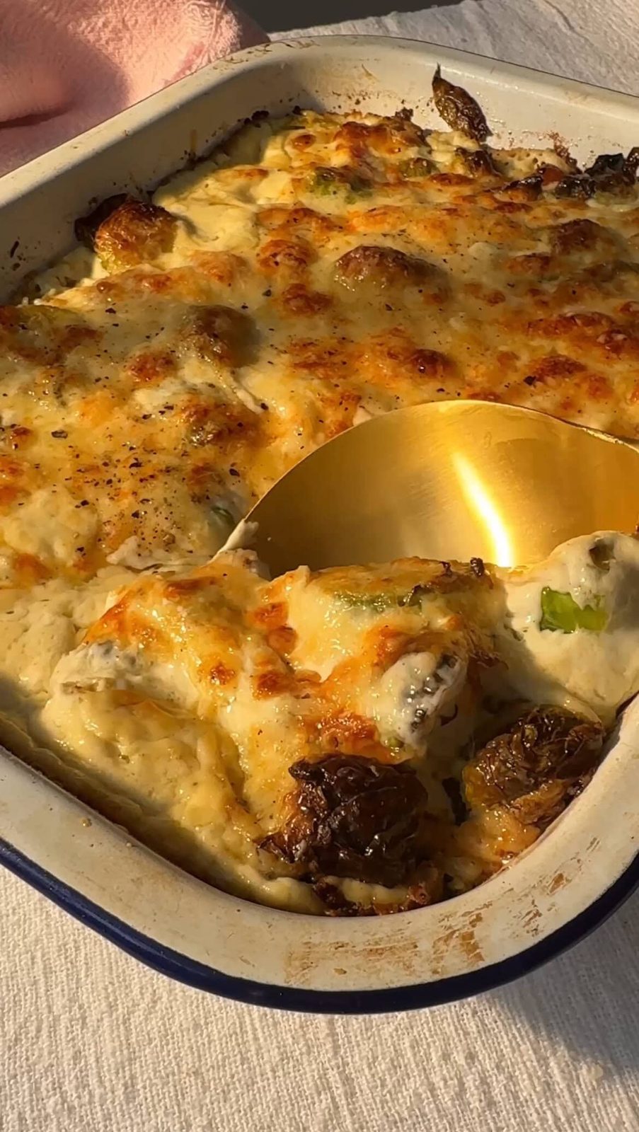 Scooping baked Brussels sprouts and bacon casserole out of pan.