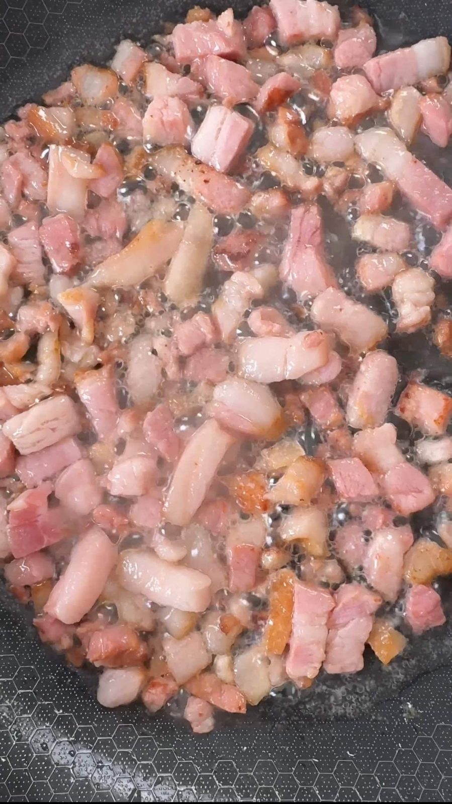 Cubed pancetta frying in a pan.
