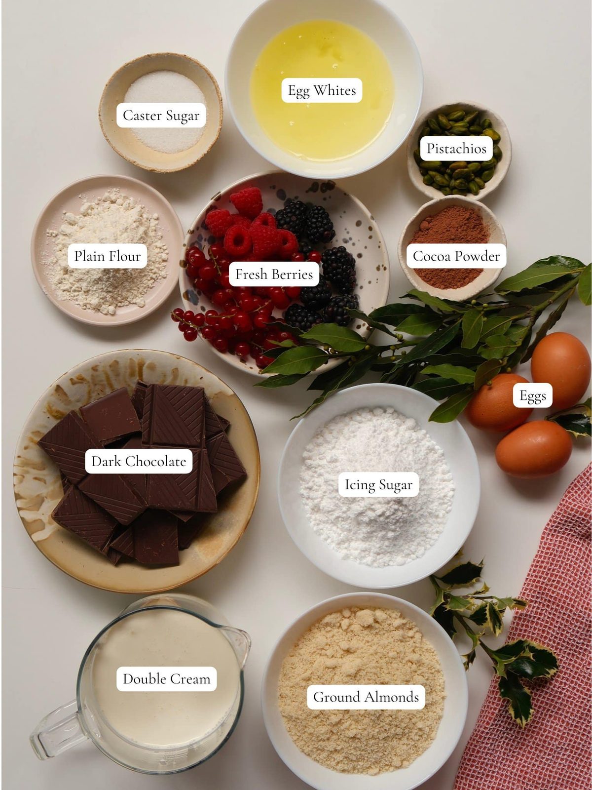 Chocolate, eggs, sugar, cream, almonds, berries, and other yule log ingredients on table.