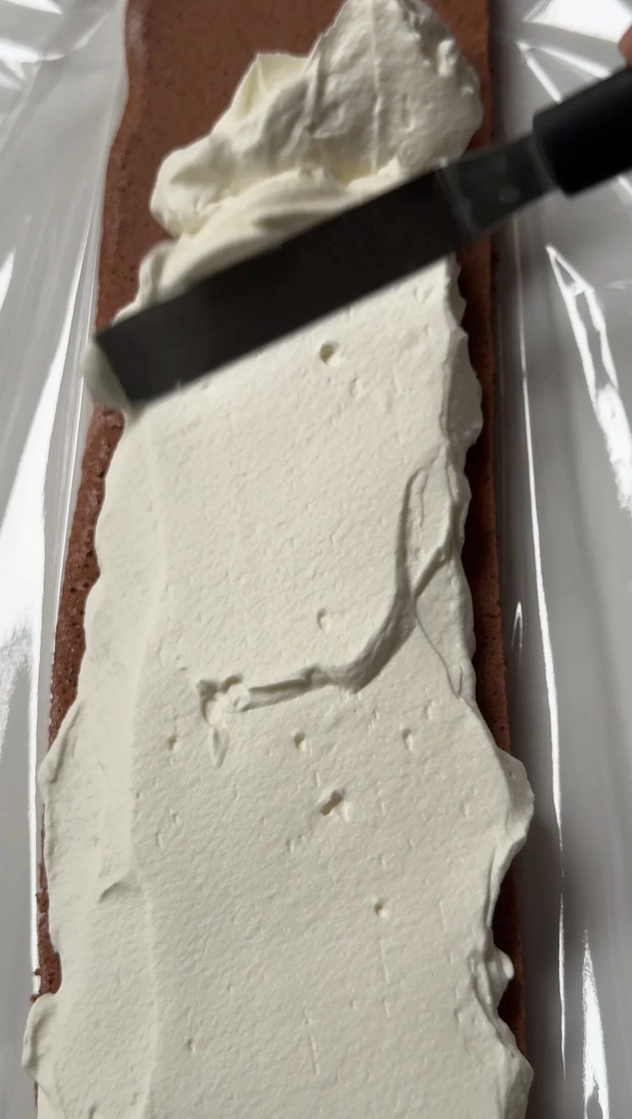 Spreading whipped cream on the yule log cake.