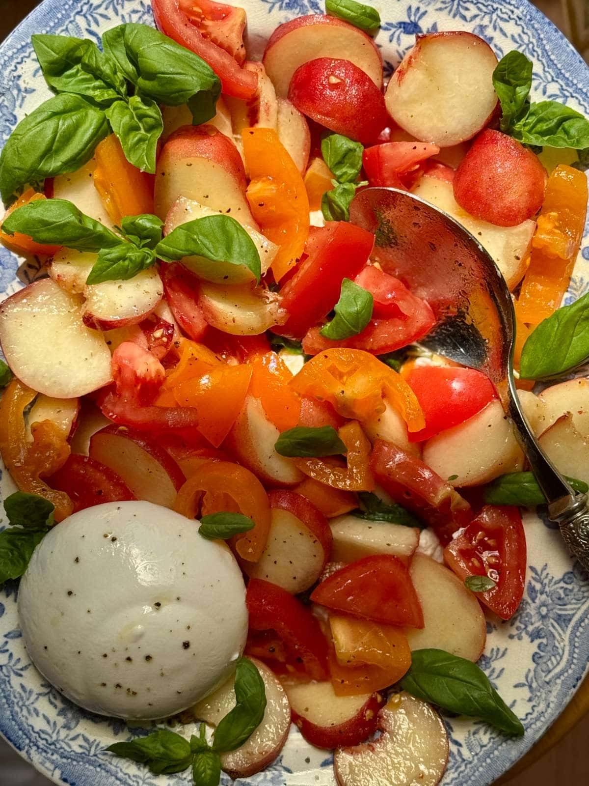 burrata and peach salad on a blue floral plate.