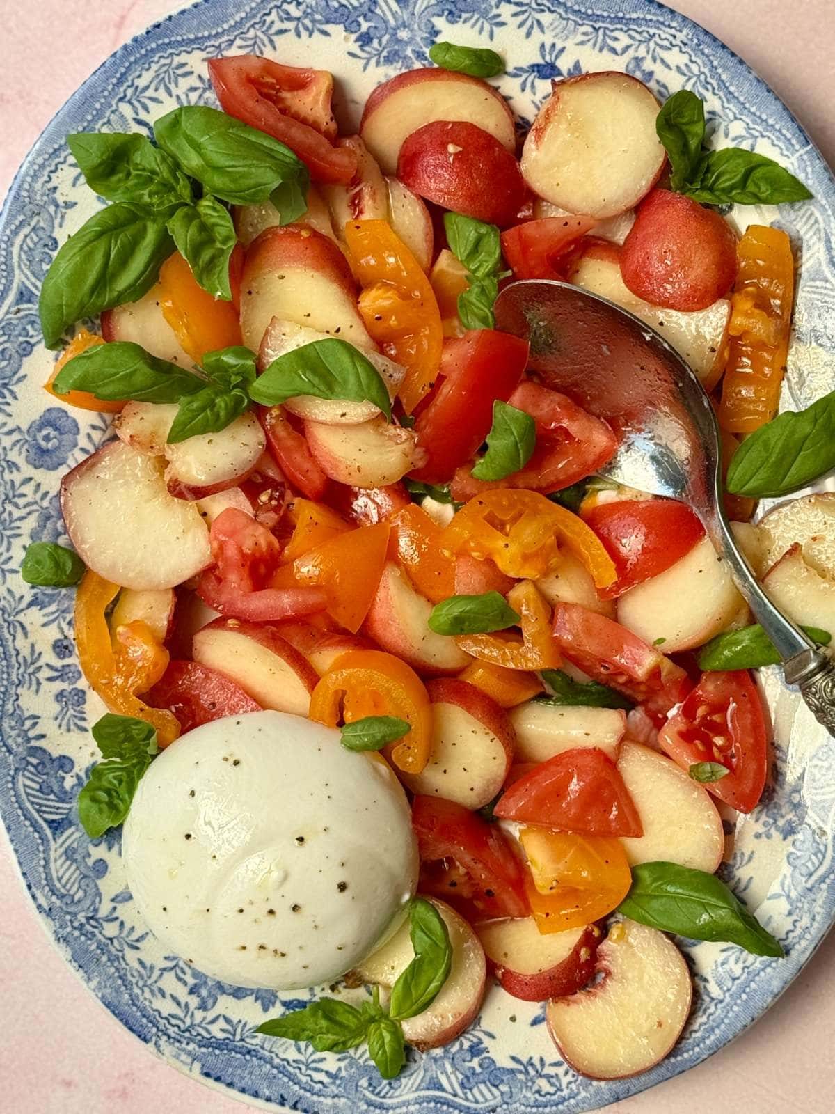 burrata and peach salad on a blue floral plate.