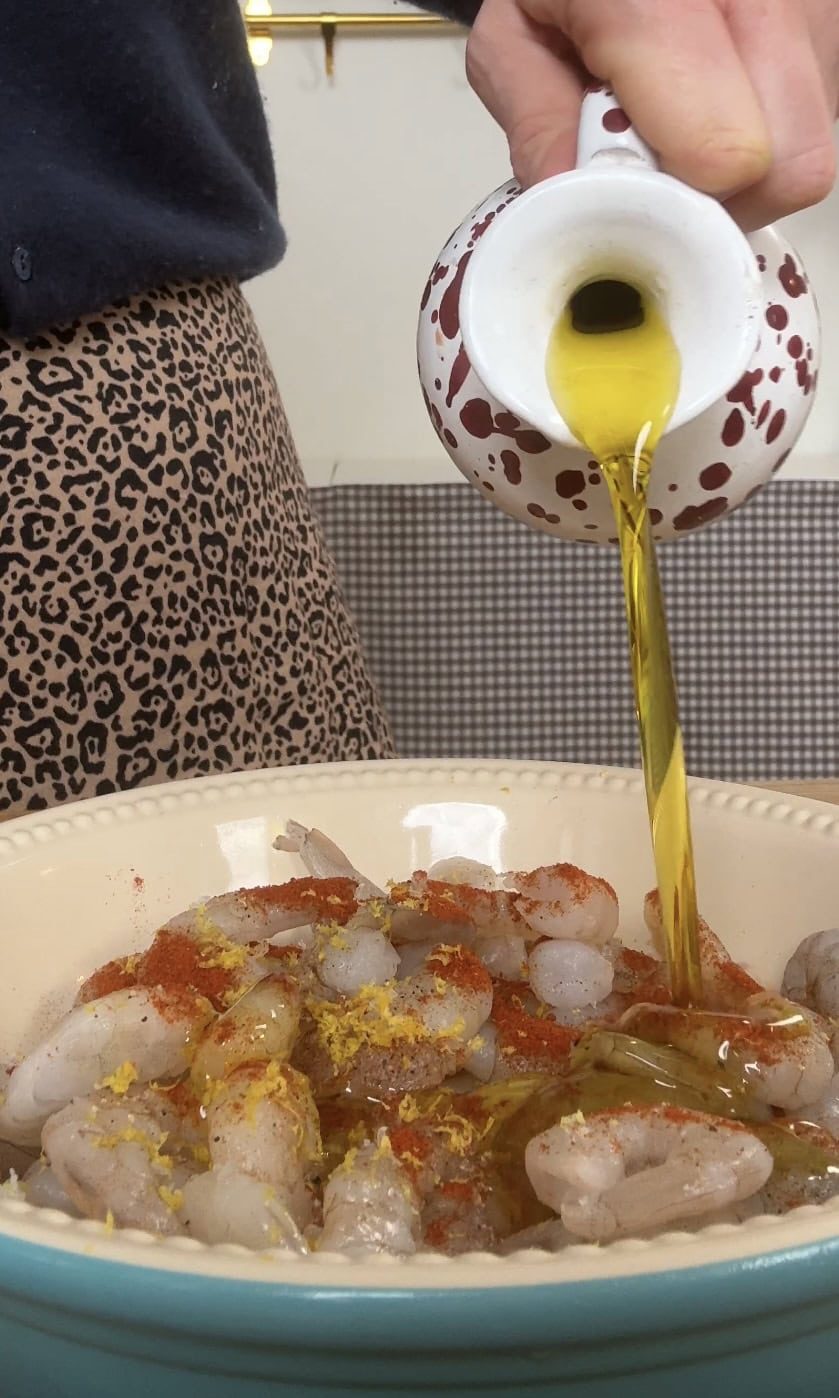 Pouring olive oil over spiced prawns.