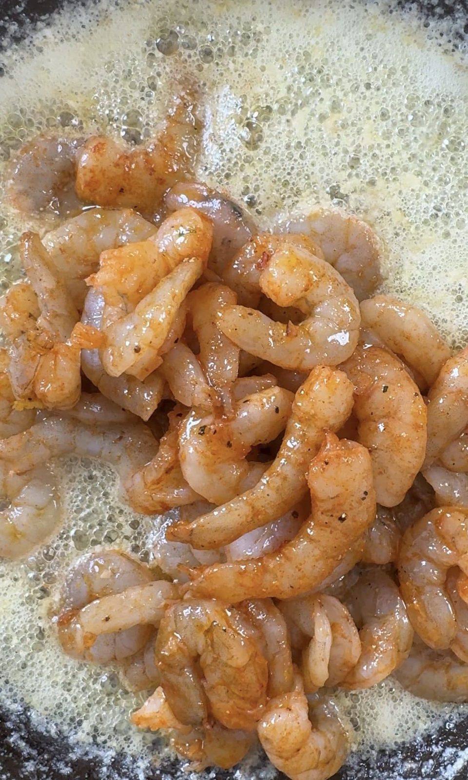 Adding prawns to the butter in the pan.