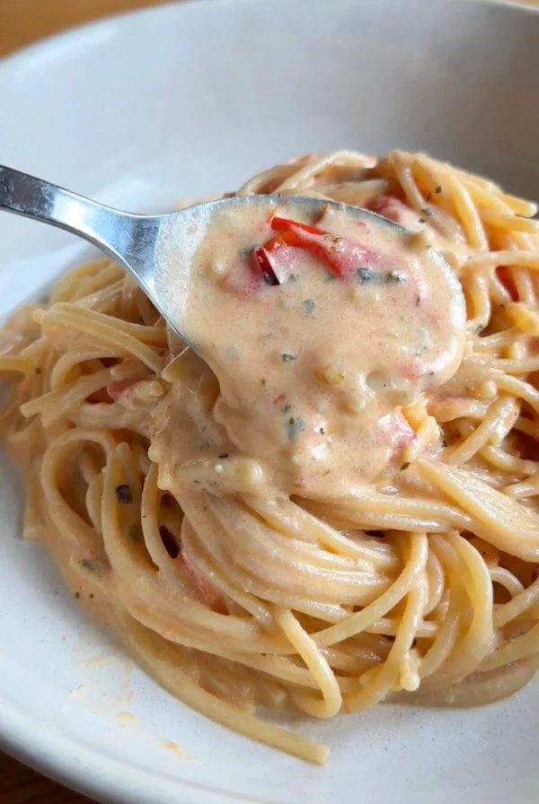 spooning creamy sauce over the boursin tomato pasta