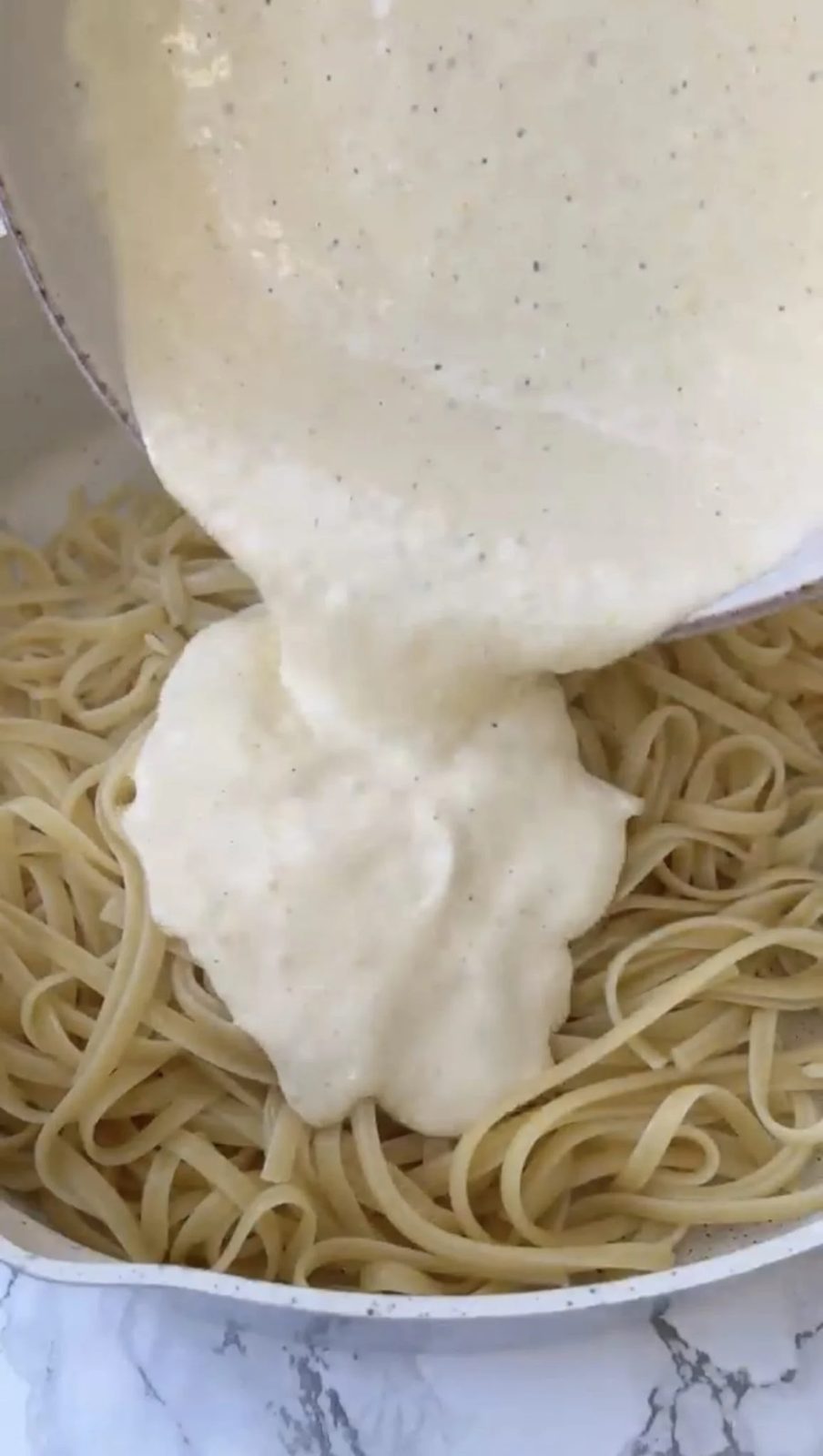 Pouring a creamy lemon sauce into pasta