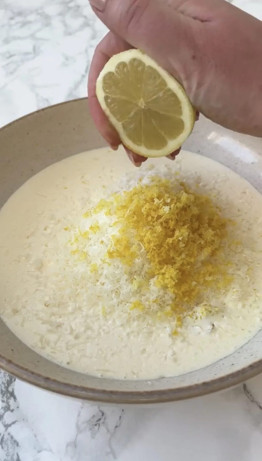 A woman squeezing lemon juice into a bowl of cream with parmesan and lemon zest