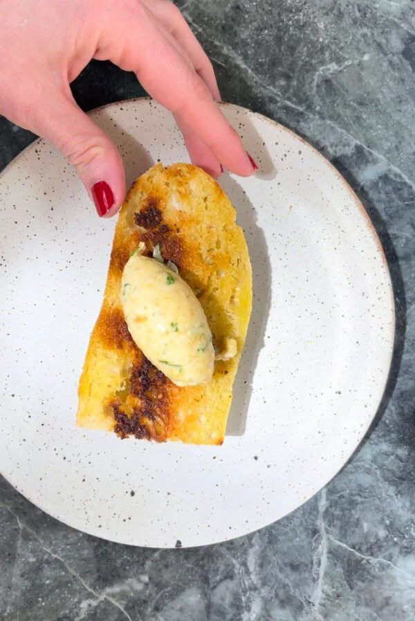 Woman with painted nails picking up a piece of toast with a piece of roasted garlic brown butter on the top.