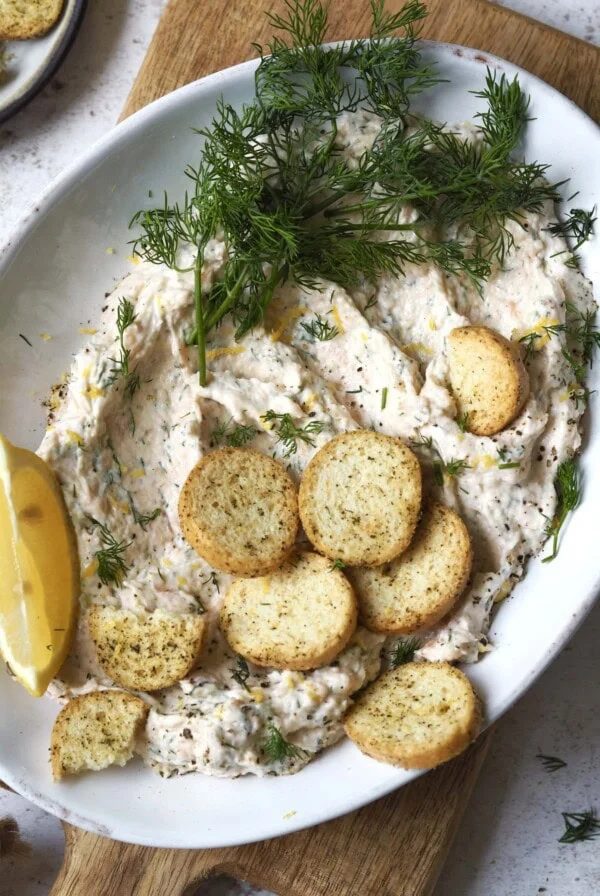 Plate of smoked salmon pate topped with fresh dill and mini crostini.