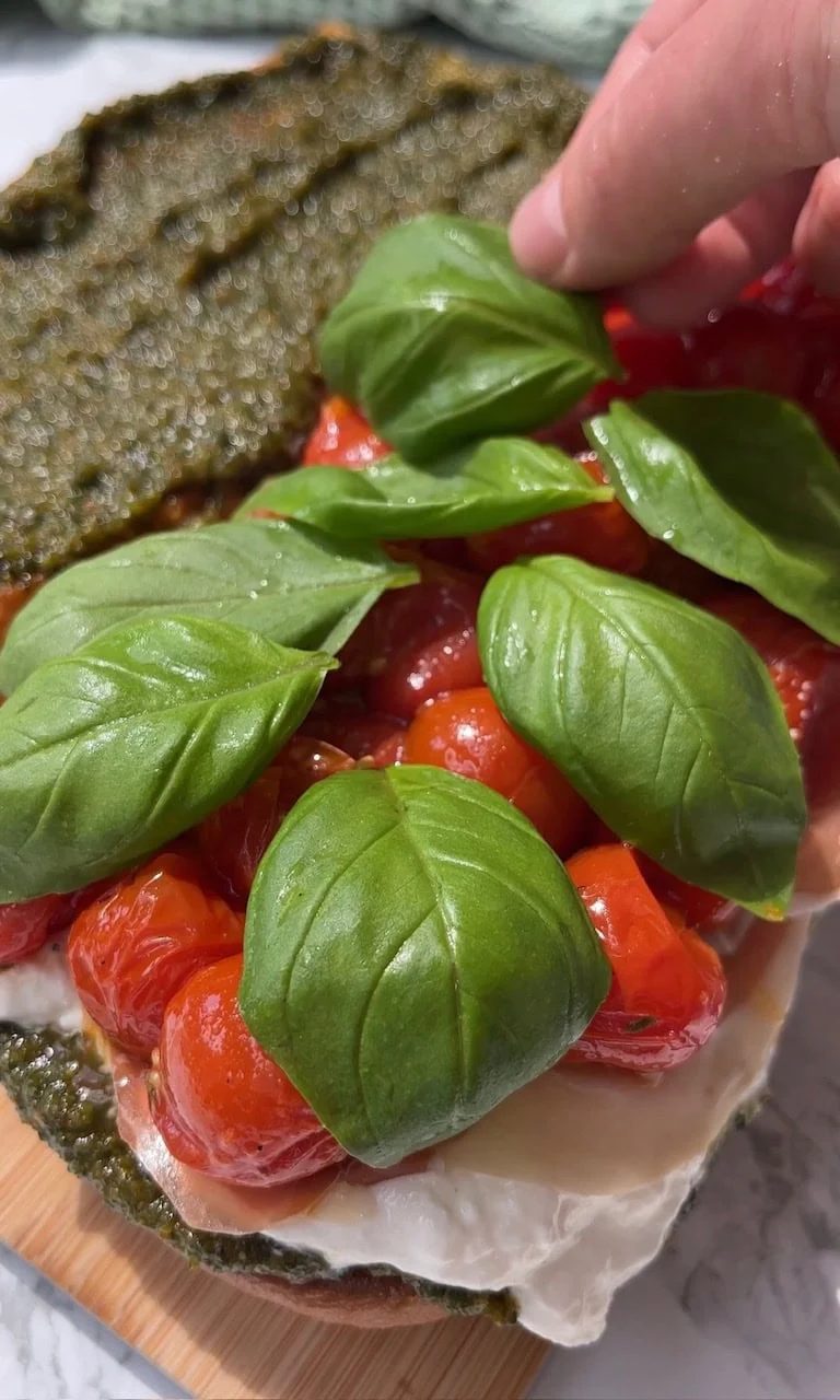 adding whole basil leaves to burrata caprese sandwich.