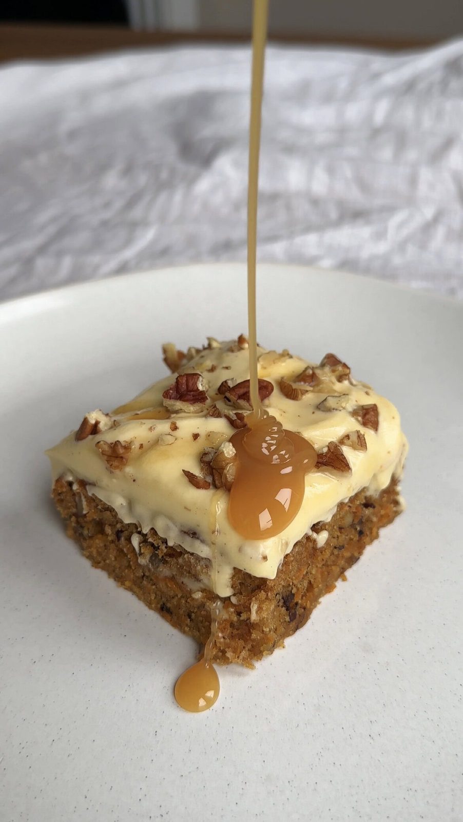 drizzling caramel sauce on a slice of carrot cake tray bake.