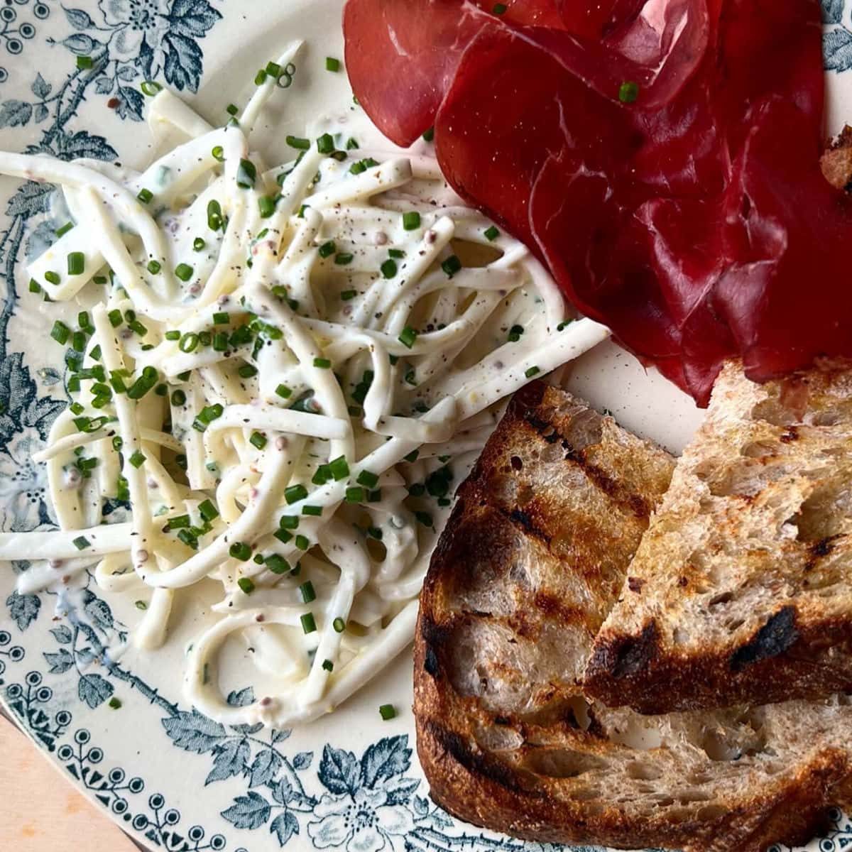 celeri remoulade on plate with bread and cured meats.