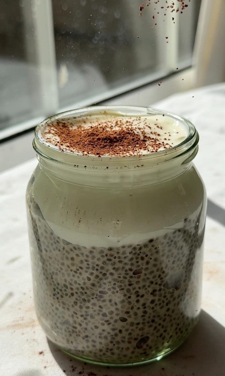 dusting cocoa powder over chia pudding with yogurt.