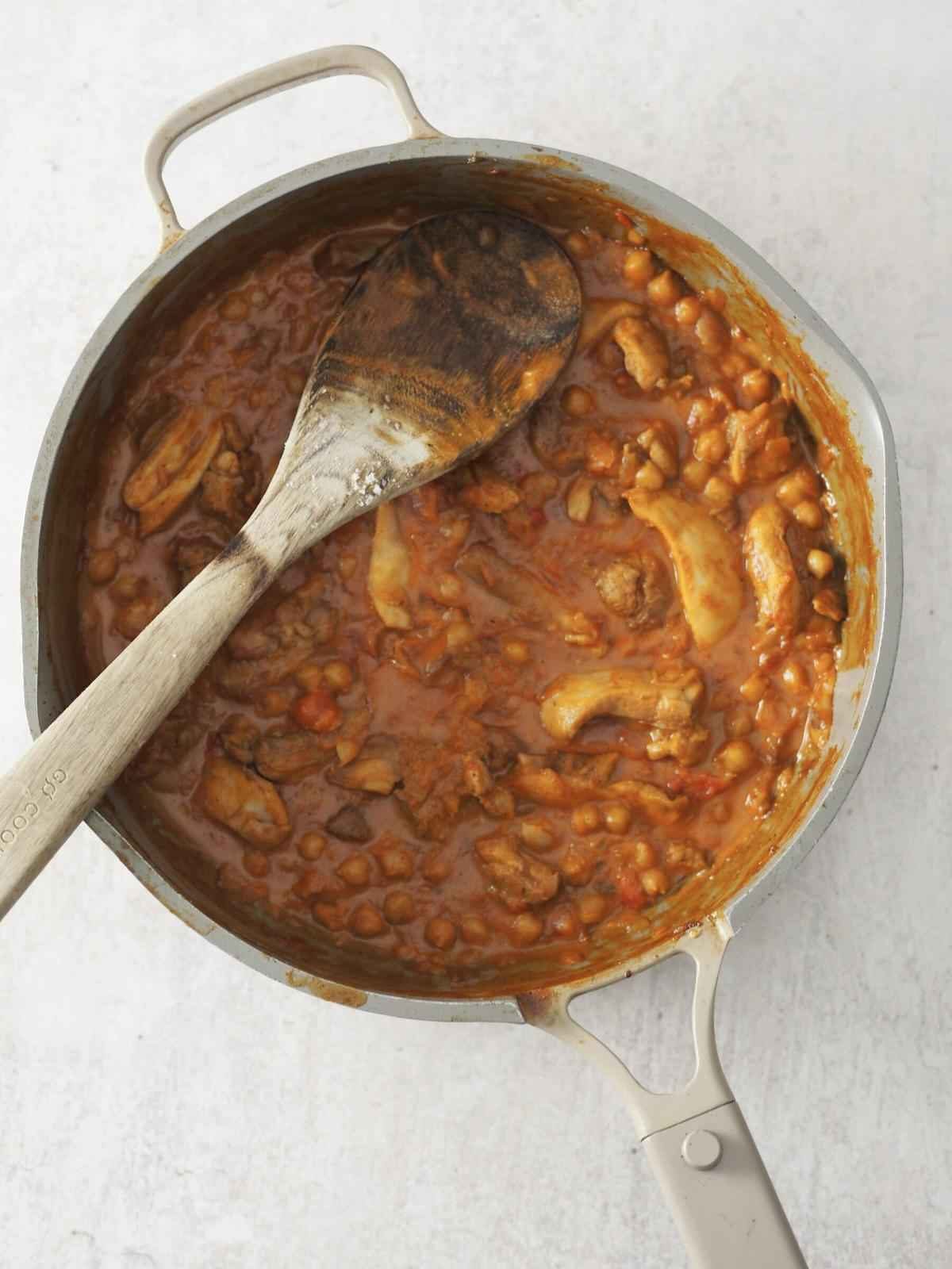 stirring the chicken and chickpea curry together.