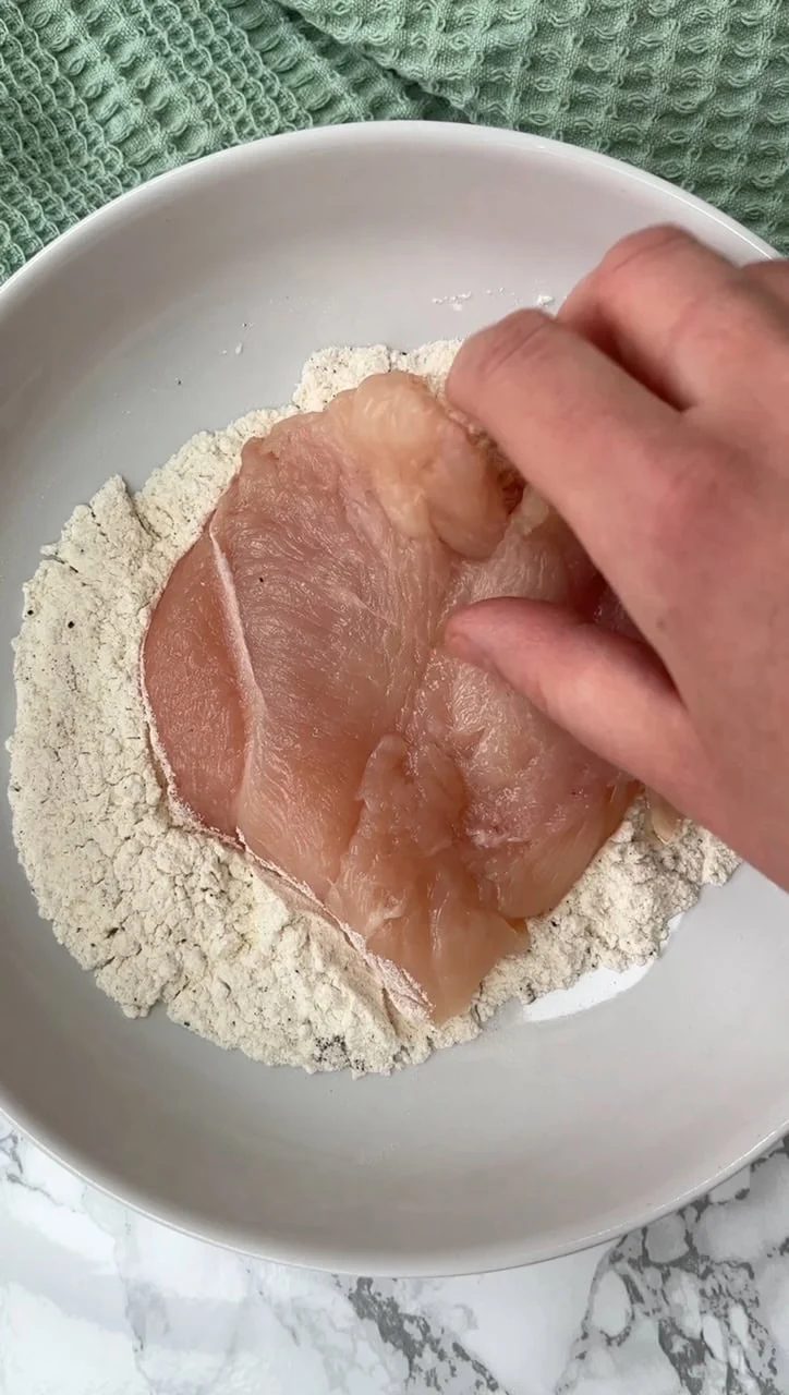 Dredging chicken breast in flour.