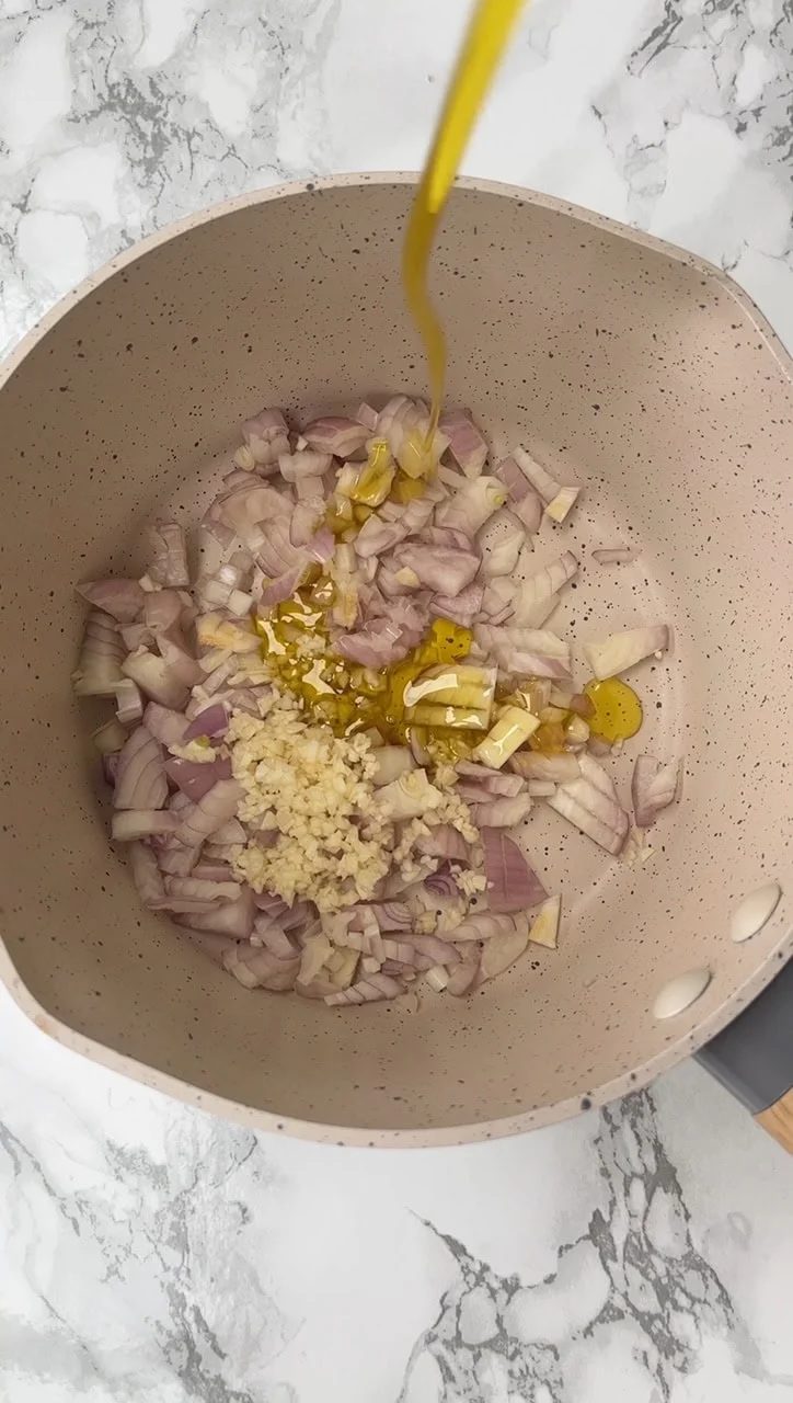 Pouring olive oil over chopped red onion in pan.