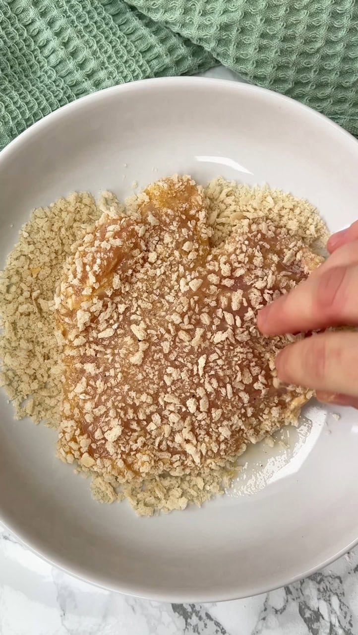 Breading chicken breast with breadcrumbs in bowl.
