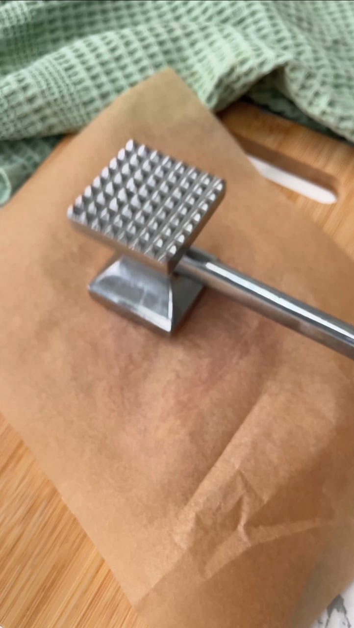 Pounding chicken breast with mallet under parchment paper.